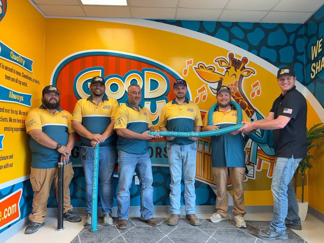 The Good Golly Garage Doors Austin team in branded shirts in front of the painted Good Golly mural at their shop, holding a high-cycle spring