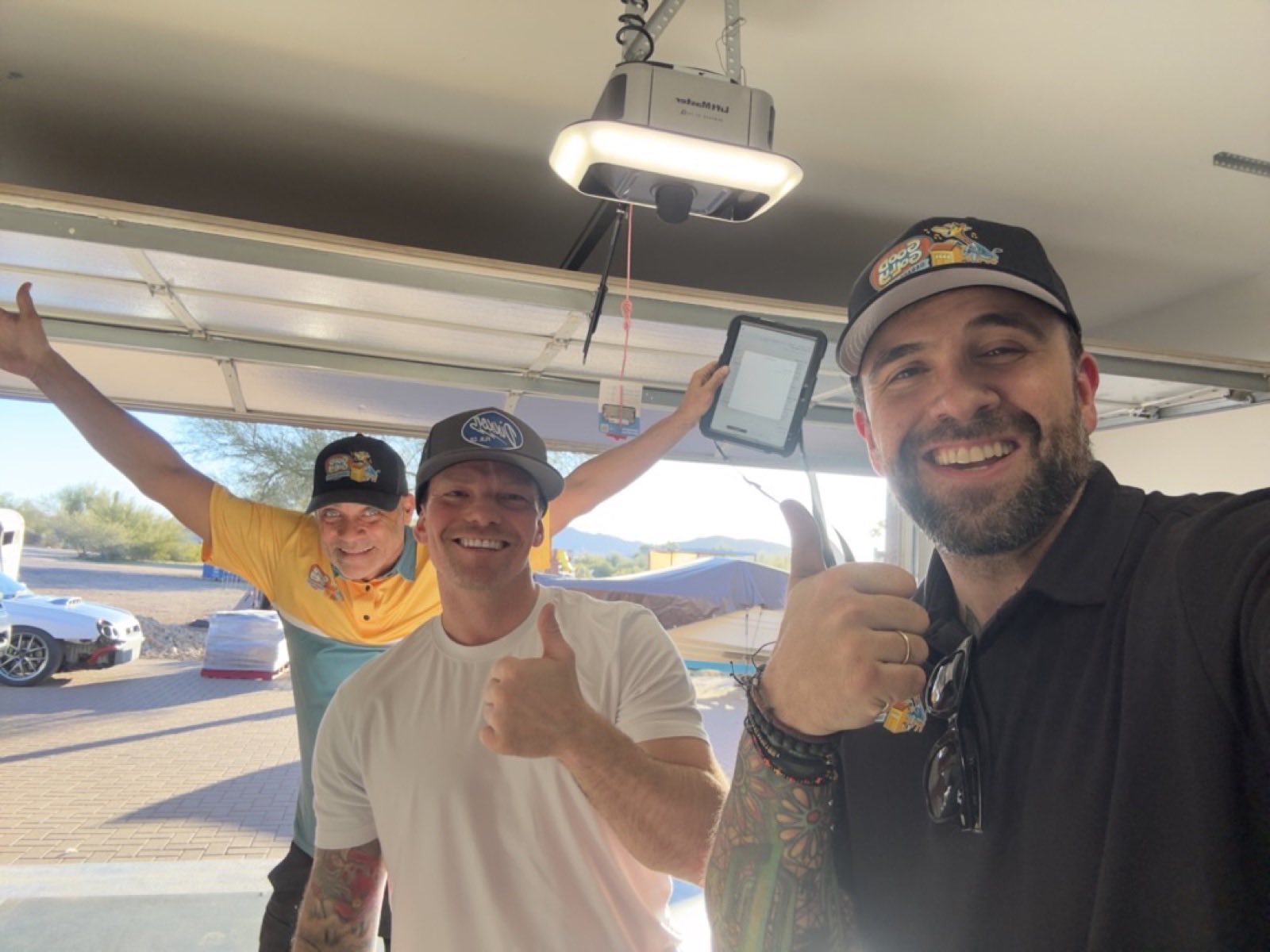 Three Good Golly team members giving a thumbs up beneath a newly installed LiftMaster opener in an open Phoenix garage, the desert visible through the doorway