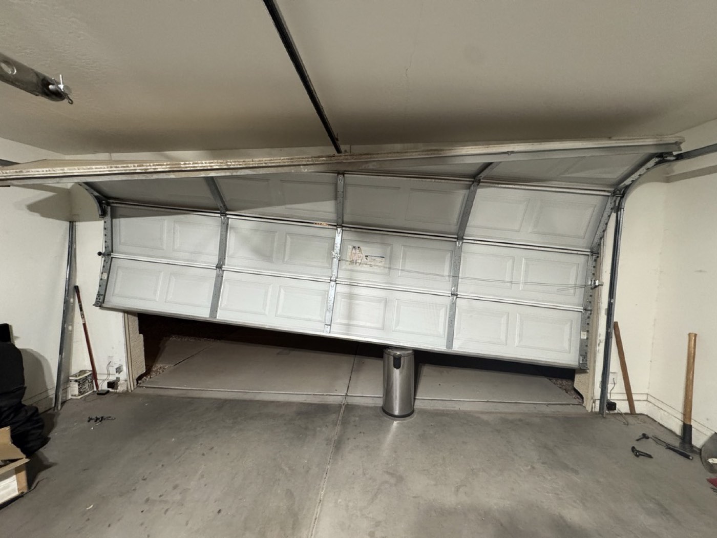 A Phoenix residential garage door hanging off its track with the bottom section buckled, before repair