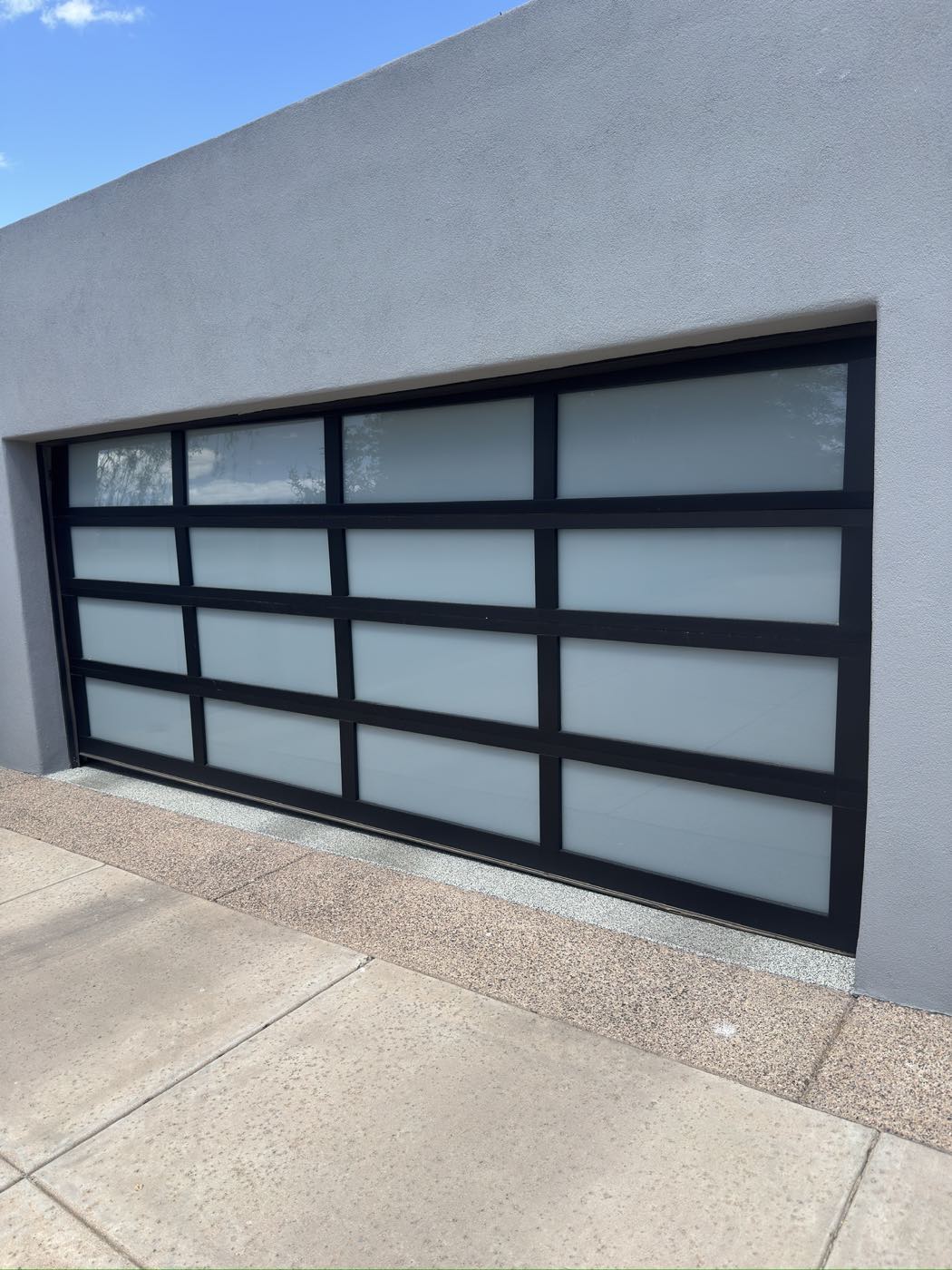 A black full-view garage door with frosted glass panels on a modern grey stucco Phoenix home