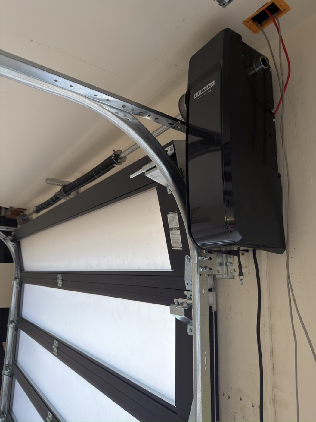 A LiftMaster wall-mount opener installed beside a Phoenix garage door with the torsion spring and track visible