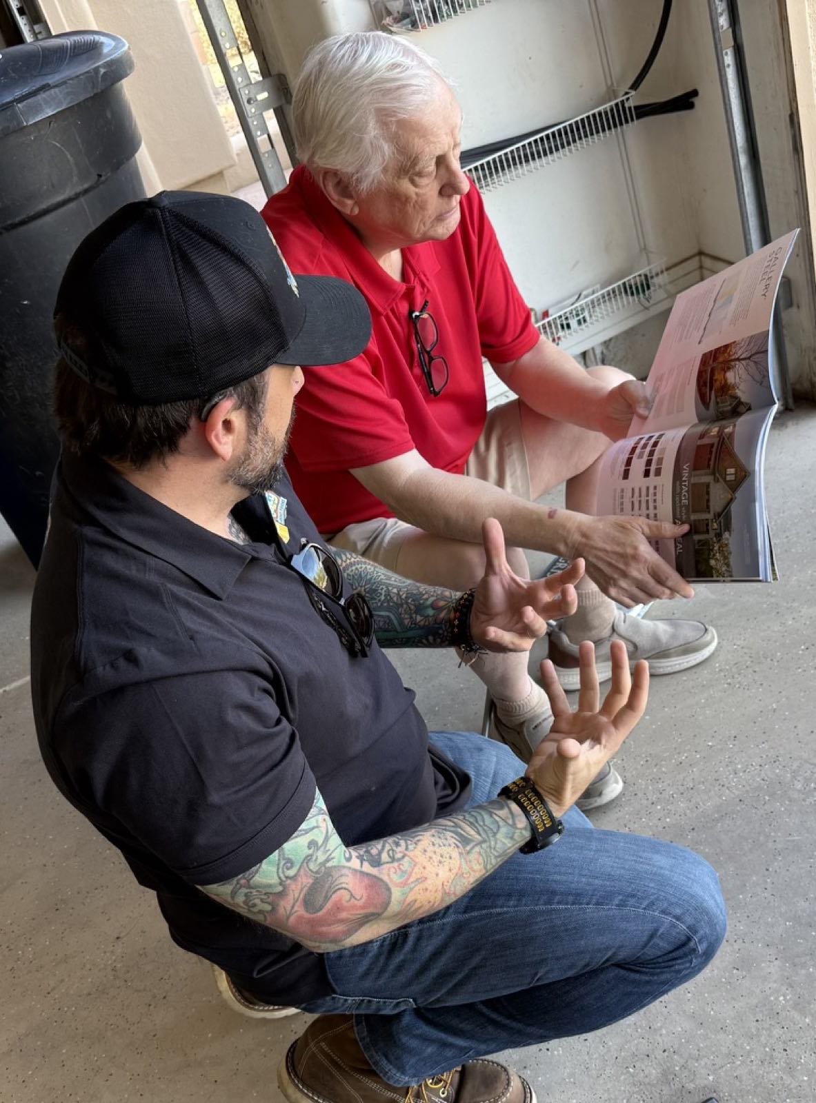 A Good Golly technician crouched beside a Phoenix homeowner in an open garage, going through a door catalogue together page by page