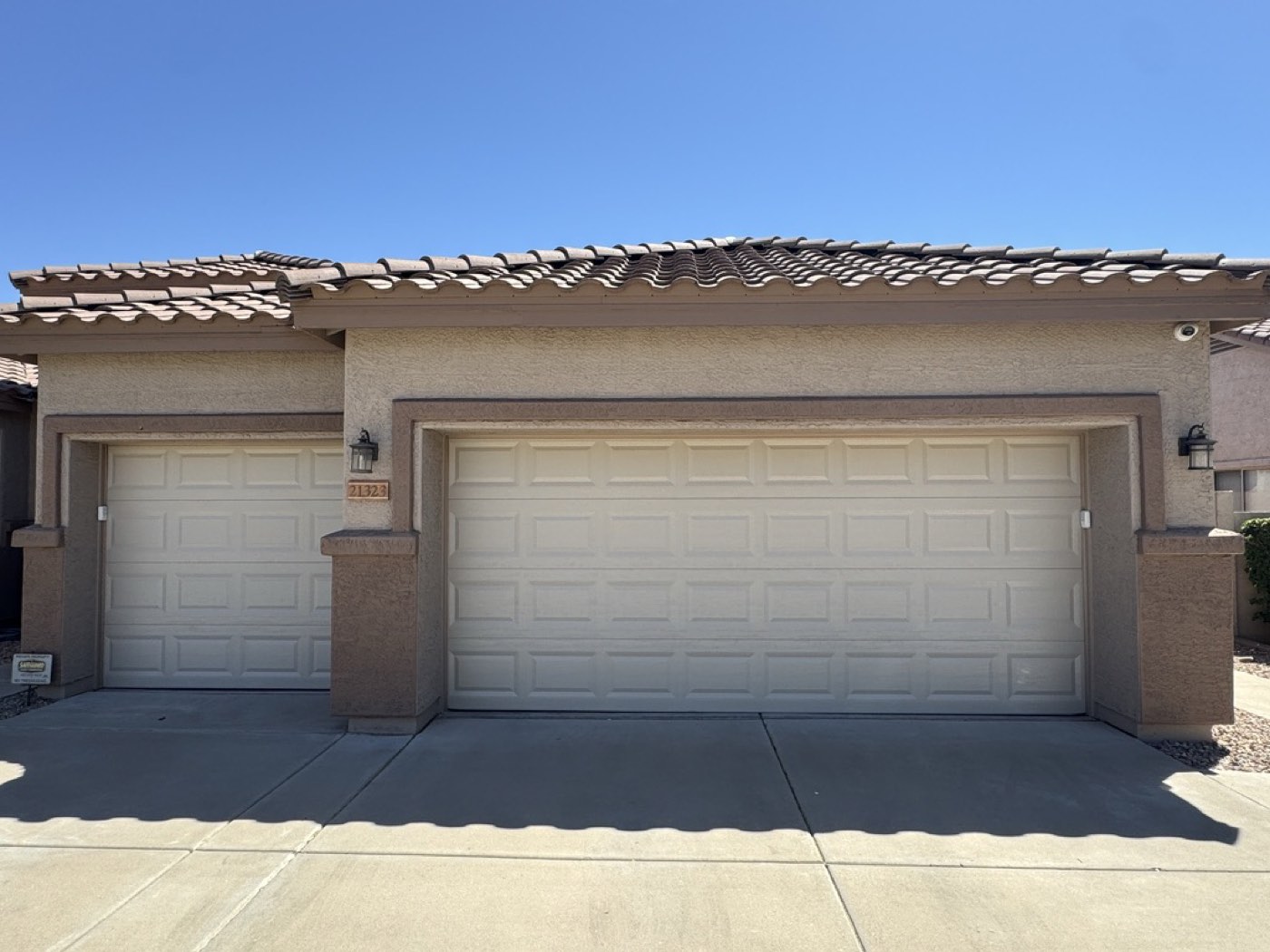 A tan raised-panel double garage door and matching single door on a tile-roof Phoenix home