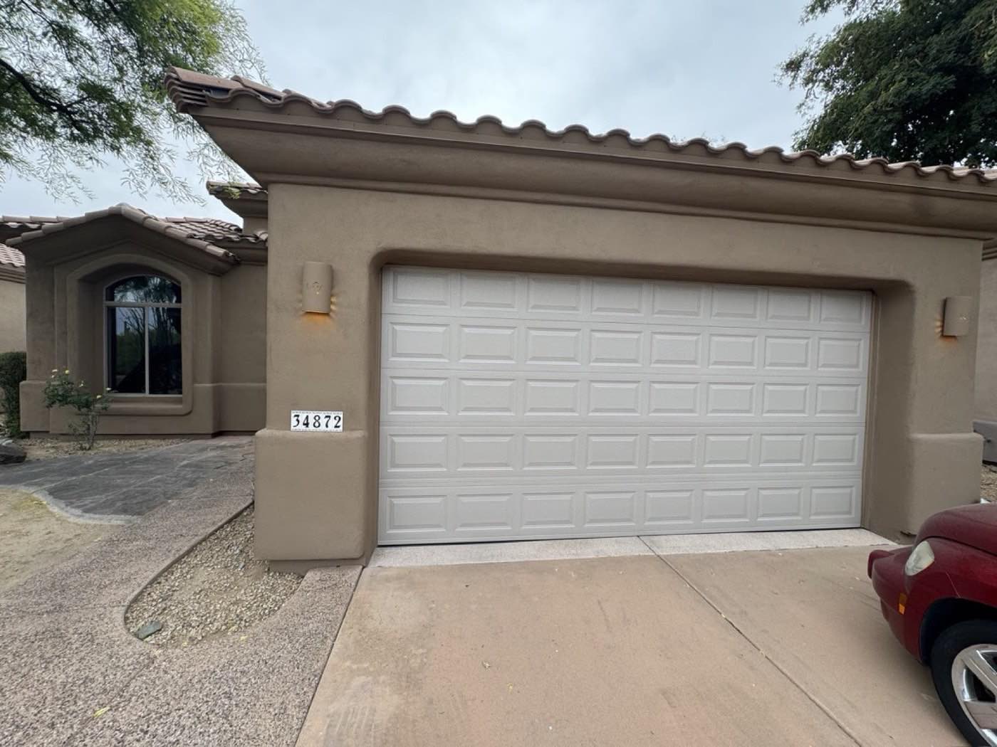 A white short-panel double garage door on a tan stucco Phoenix home with a clay tile roof