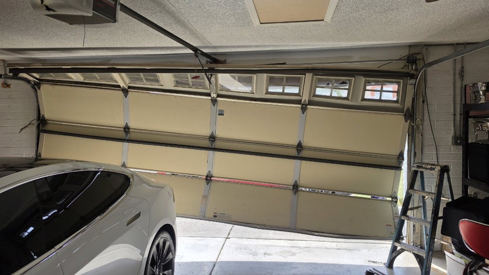 An almond garage door with a top row of windows seen from inside a Phoenix garage during a service call, with a step ladder standing at the right-hand track