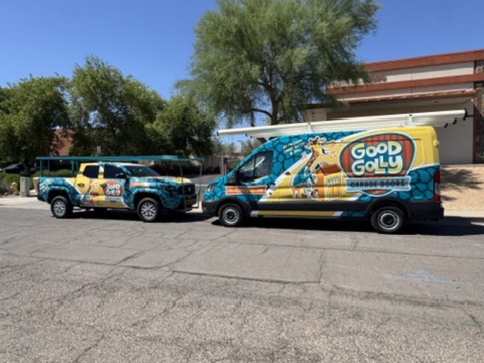 The wrapped Good Golly Garage Doors truck and van parked together on a Phoenix street under desert trees