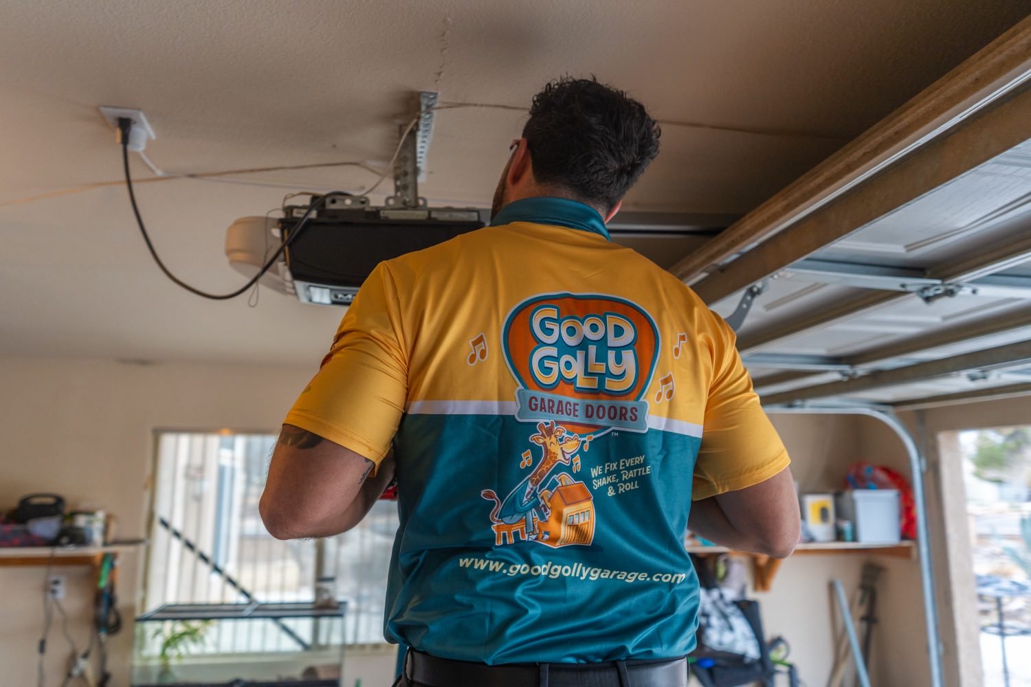 A Good Golly technician in the branded Victorville shirt standing beneath a garage door opener mid-service