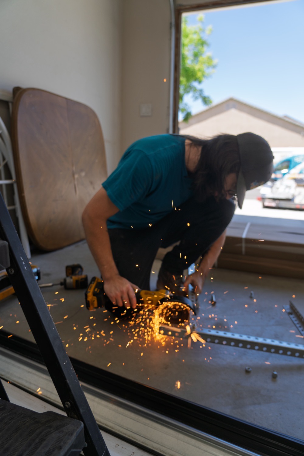 A Good Golly technician cutting garage door track with an angle grinder, sparks scattering across the floor of a Victorville garage