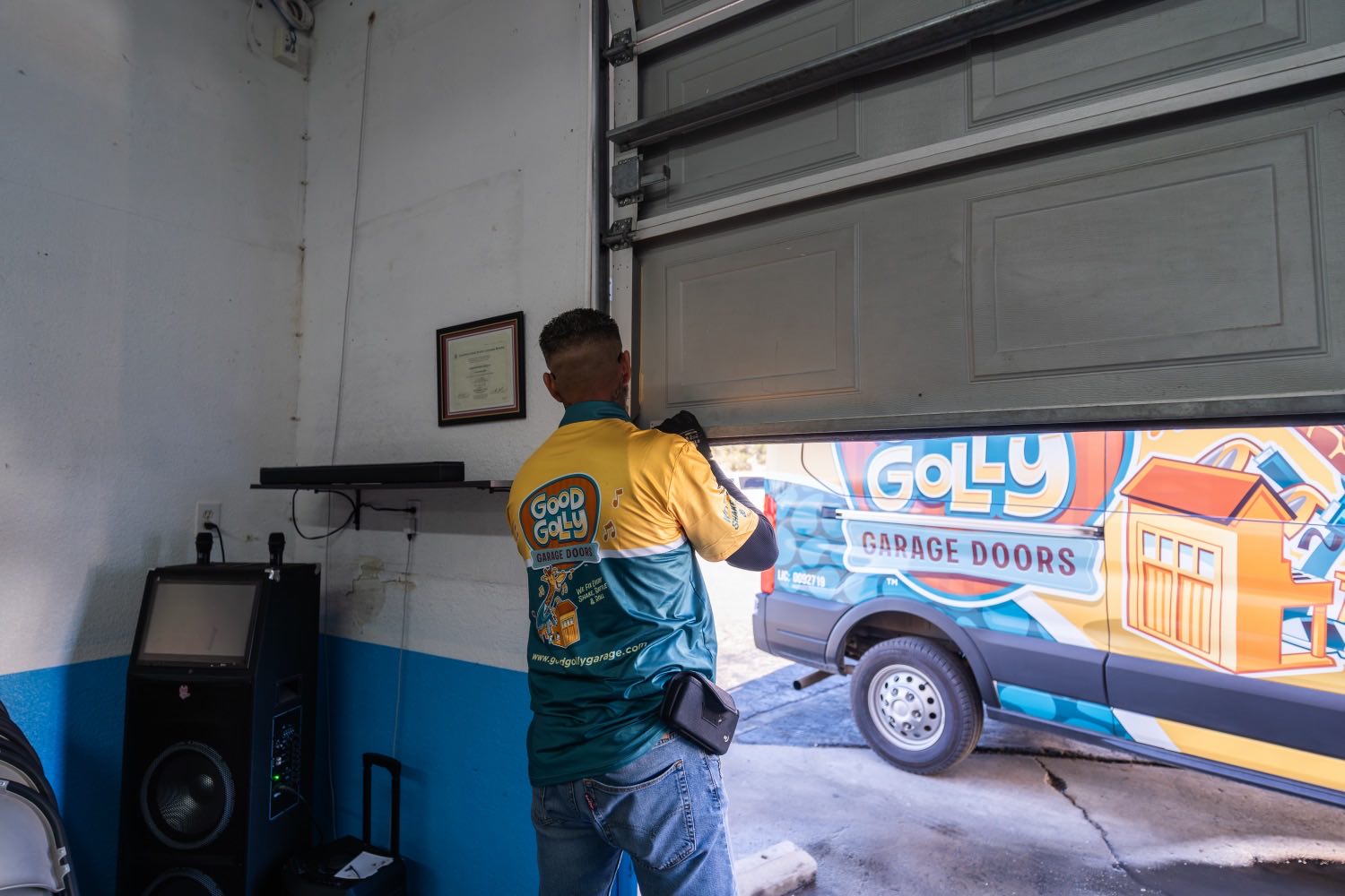 A Good Golly technician working a roll-up door at the Victorville shop with a wrapped van parked inside