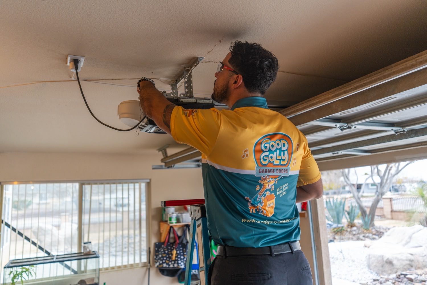 A Good Golly technician reaching up to the opener rail bracket on the ceiling of a Victorville garage