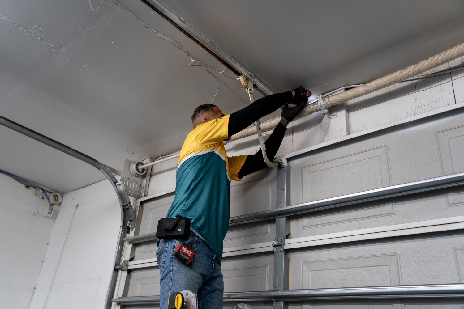 A Good Golly technician working on the cable and torsion hardware at the top of a Victorville garage door track