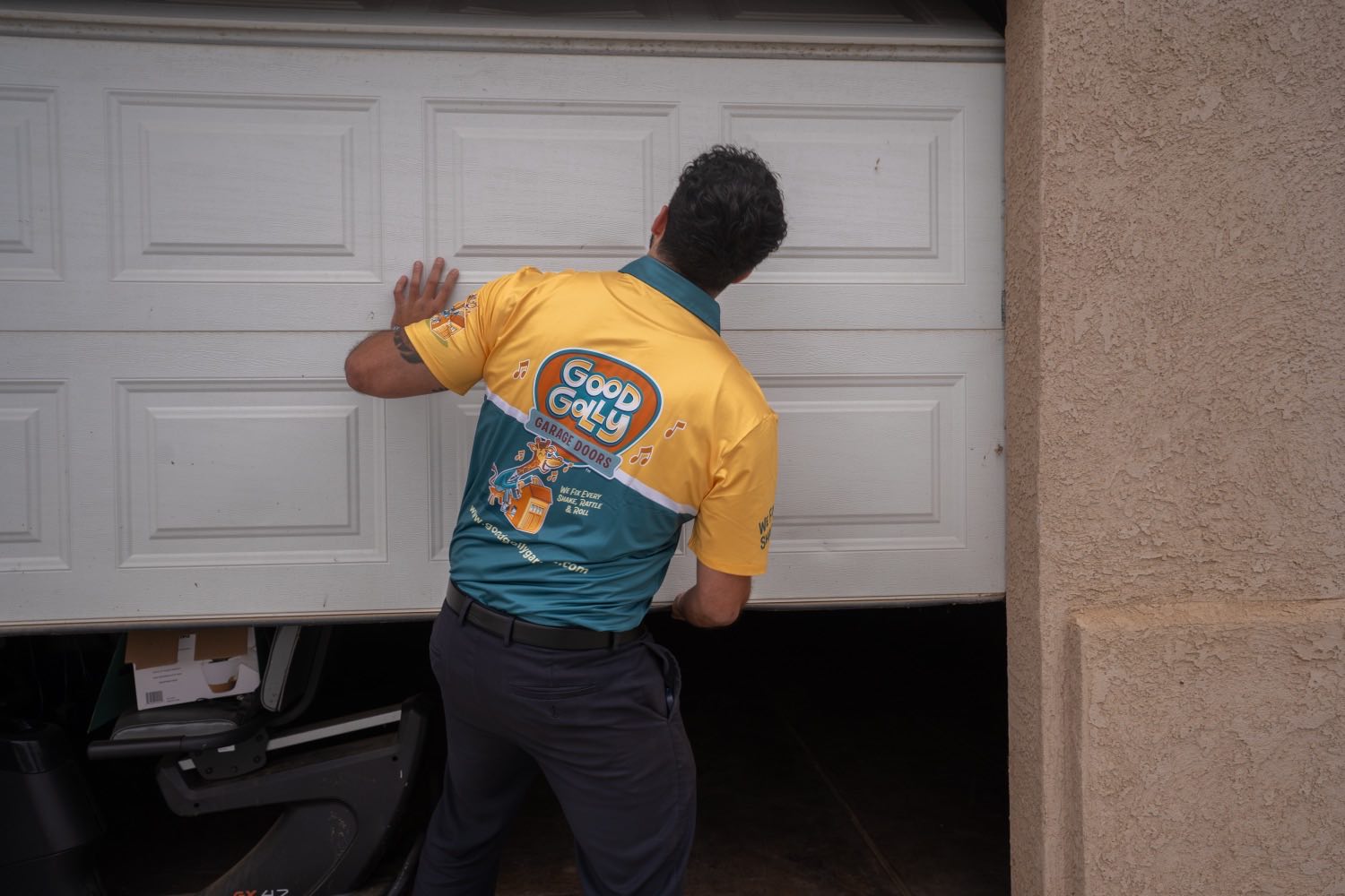 A Good Golly technician guiding a white sectional garage door down by hand at a Victorville home