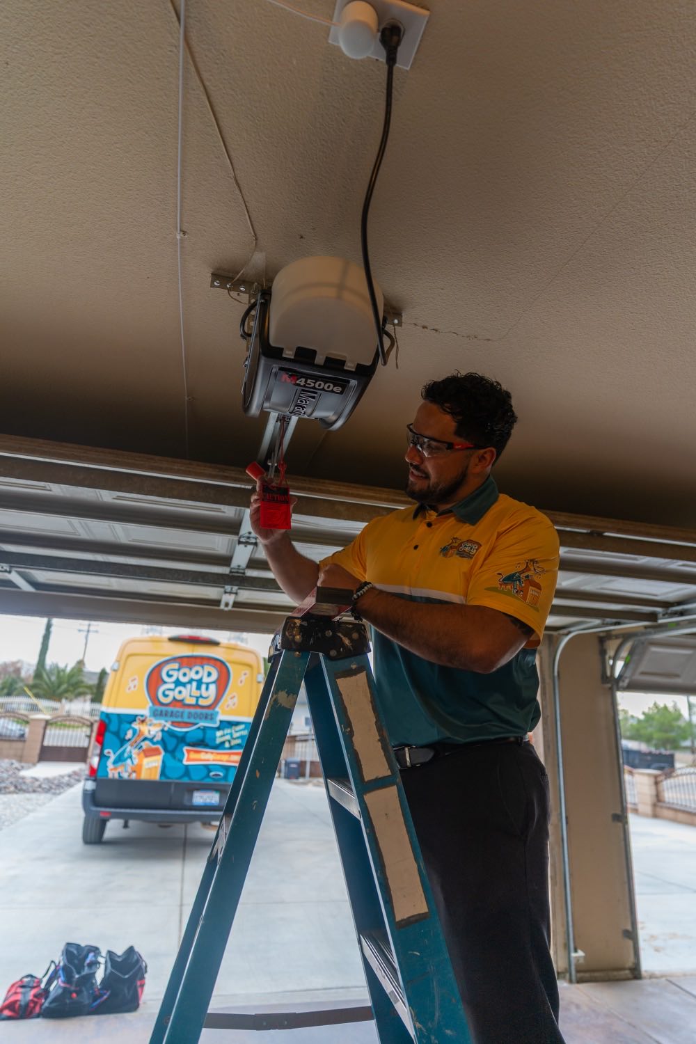 A Good Golly technician on a ladder servicing a Genie garage door opener in a Victorville garage