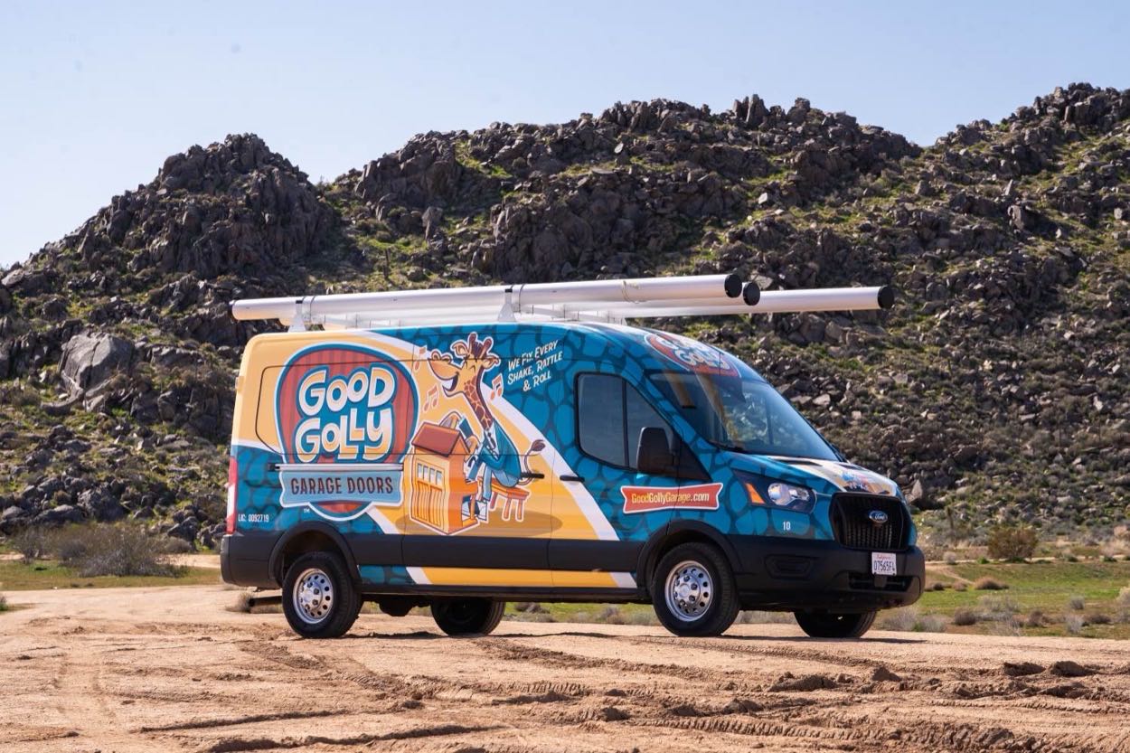 A wrapped Good Golly Garage Doors van parked on a dirt road below the rocky hills of the High Desert