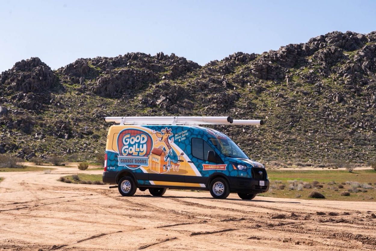 A Good Golly Garage Doors service van on a High Desert dirt road with track tubes on the roof rack
