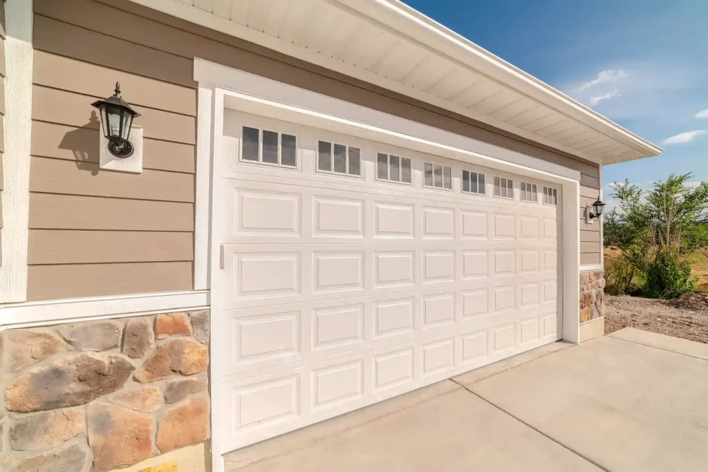 A white paneled garage door with a decorative arched frame and two black lantern lights on a gray stucco garage.