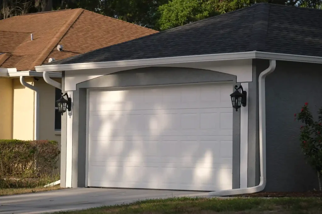 A two-car wooden garage door with an X-brace design and gridded windows on a white brick house.