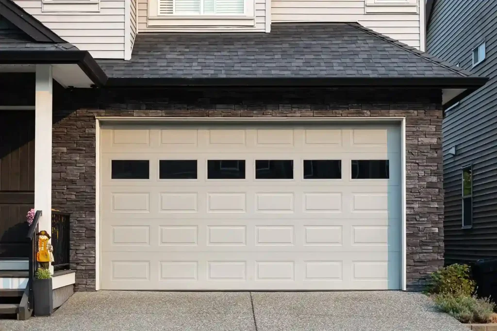 A gray paneled garage door with four white-framed windows on top, each with multiple panes.