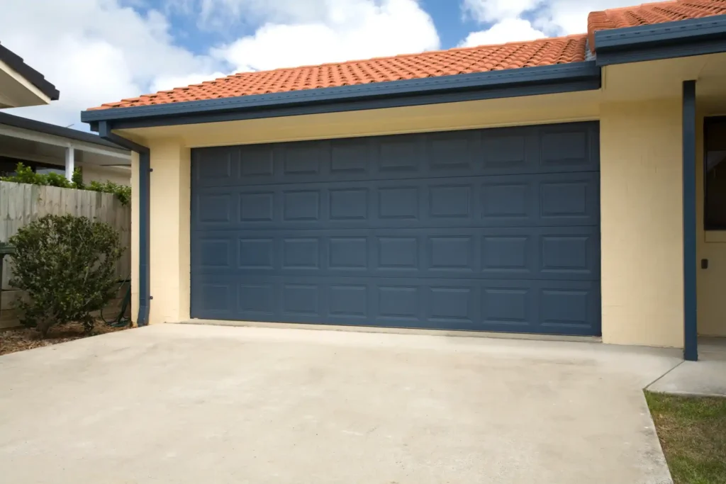 A two-car garage with a blue paneled door on a light yellow stucco house with a red tile roof.