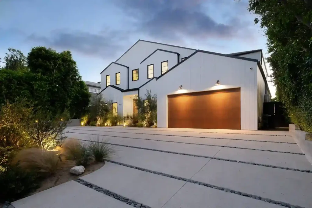 A modern, white house at dusk with a large, glossy brown garage door and minimalist landscaping.