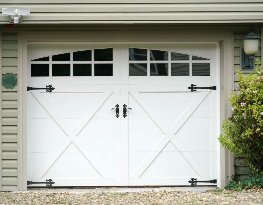 A white two-car garage door with an X-brace design and decorative black hinges, handles, and windows.