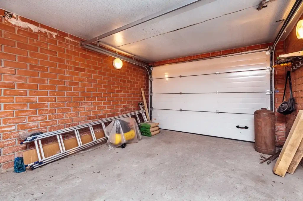 Interior view of a brick-walled garage featuring a closed white sectional garage door and a ladder leaning against the wall.