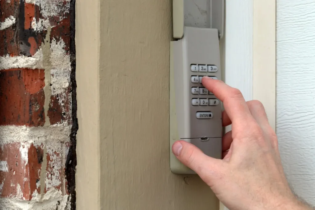 Person pressing number 3 on wall-mounted access keypad beside white door and brick wall.