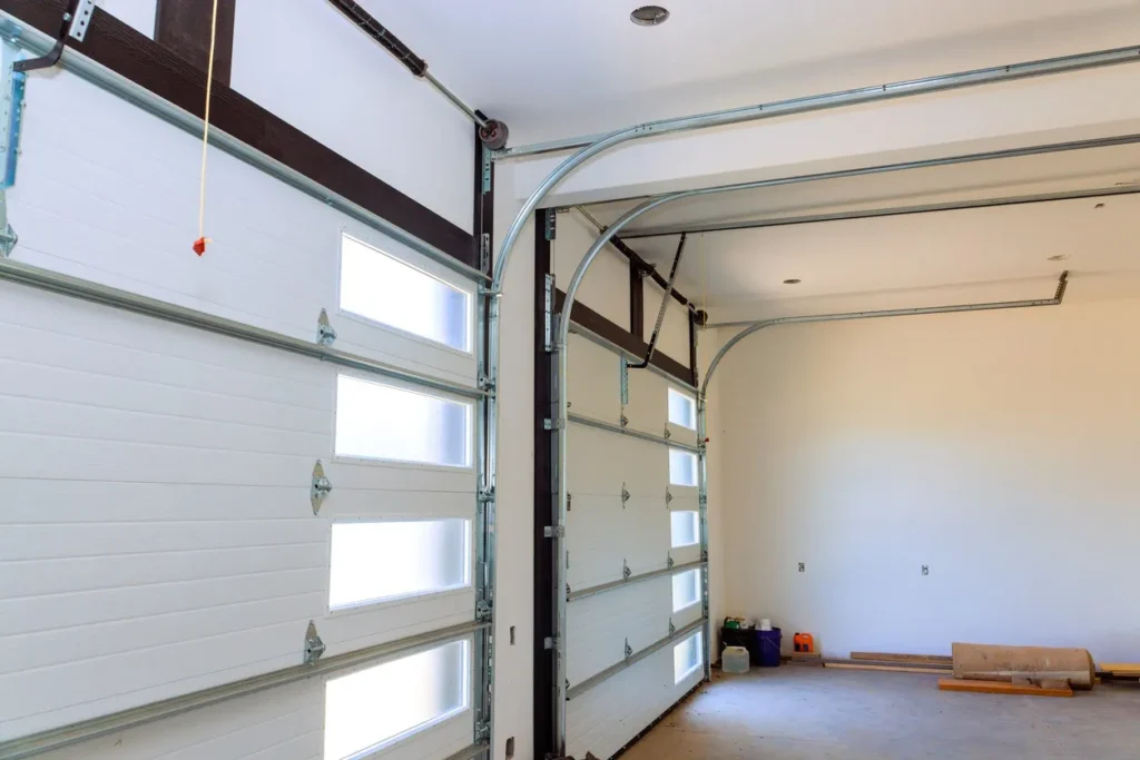 Modern residential garage interior with two sectional doors featuring frosted glass panels and torsion springs. Construction materials on floor.