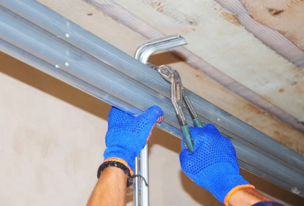 Person in blue gloves using pliers to adjust metal conduit along ceiling with exposed insulation and beams.