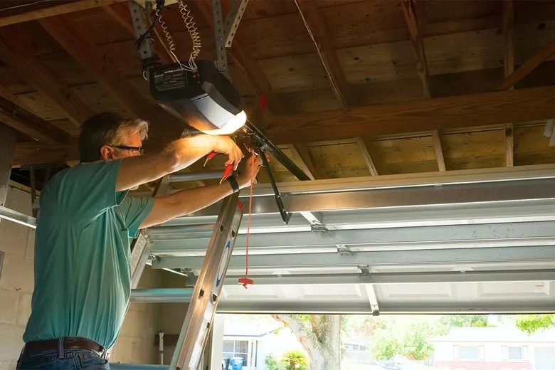 Man on ladder repairing garage opener.