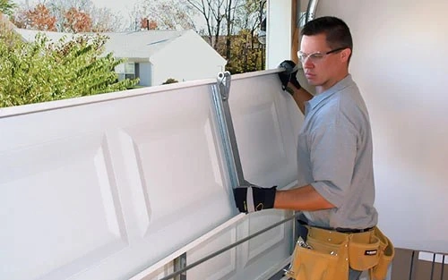 Technician installing white garage door panel.